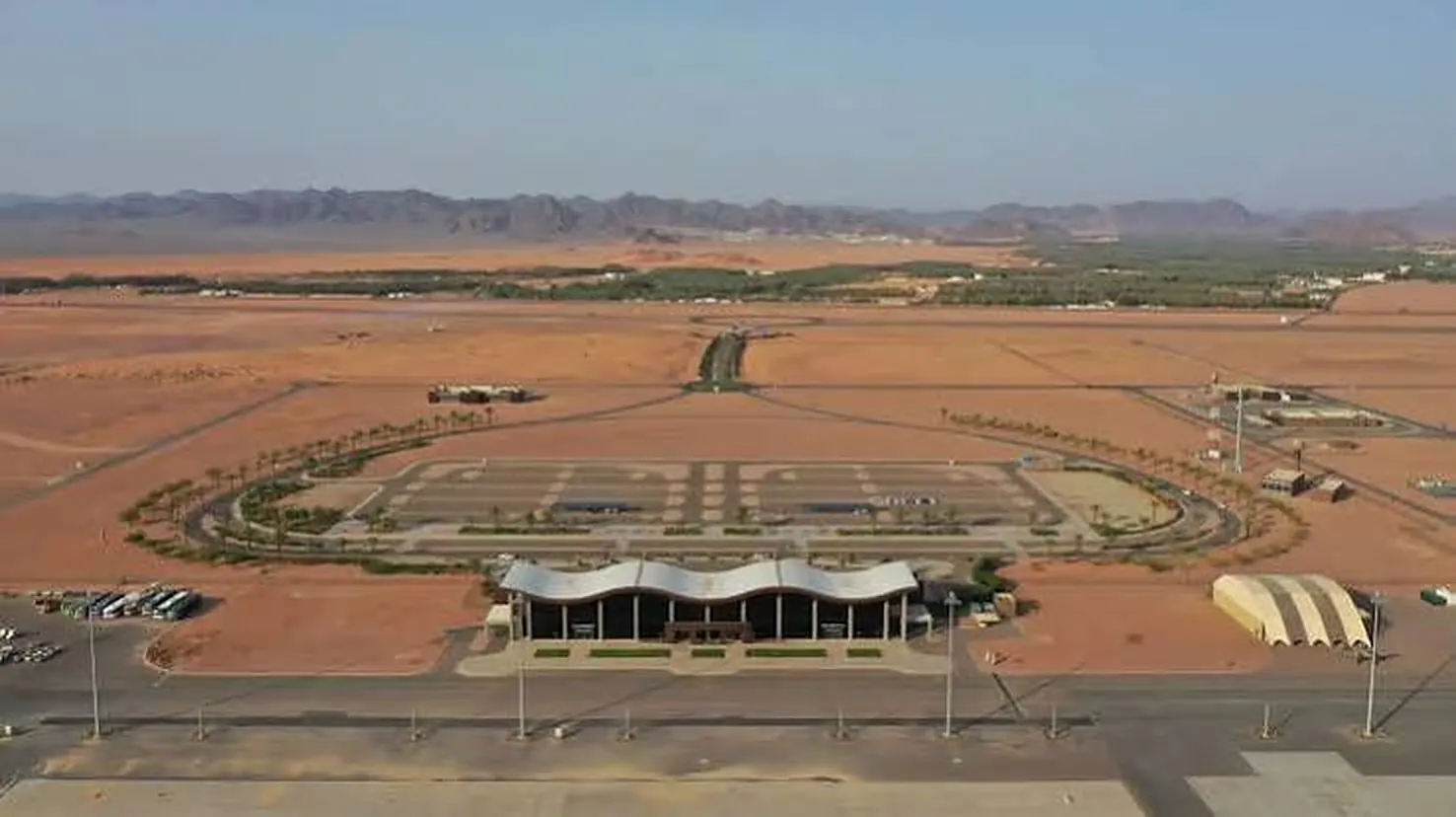 Aerial view of the AlUla airport terminal and forecourt in the desert, with mountains in the distance
